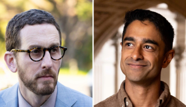 A man with glasses, a beard, and a blue suit looks seriously to the side, while a clean-shaven man in a brown shirt smiles gently against an arched background.