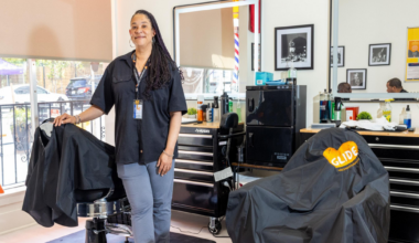 A person is having their hair cut with electric clippers near the side of their head, while wearing a black glove.