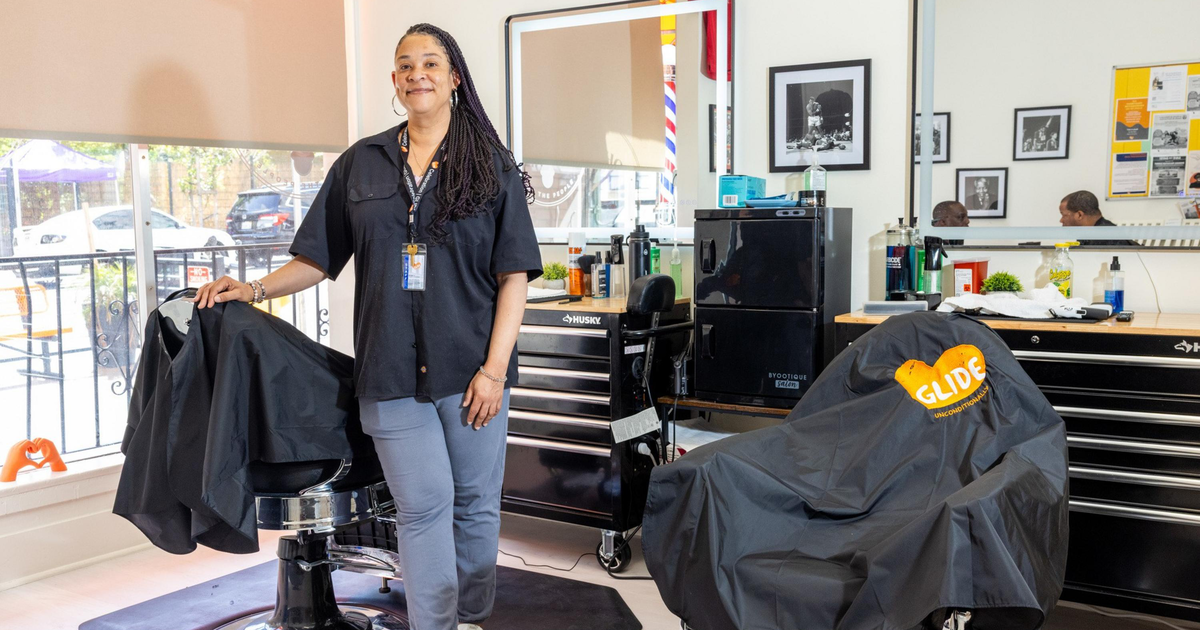 A person is having their hair cut with electric clippers near the side of their head, while wearing a black glove.