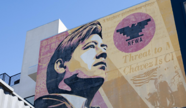 A large mural of a young man looking upward with the NFW logo and faded text about Chavez and farm workers is painted on a building.