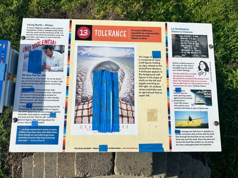 A sign with photos and text about Cesar Chavez. Someone has covered images of Chavez and references to him with blue painters tape