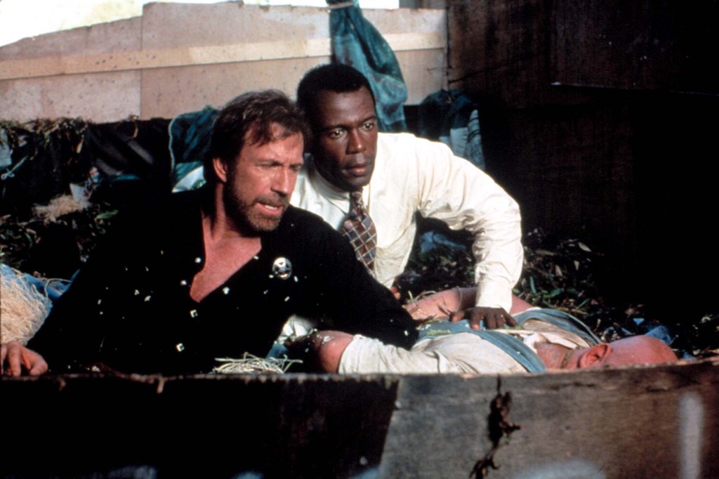 Chuck Norris and Clarence Gilyard Jr. looking down at a third person lying in what appears to be a ditch.