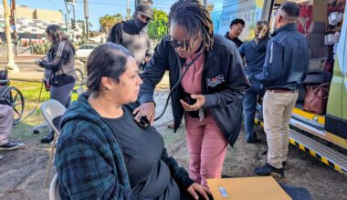 A street medicine nurse holds the end of a stethoscope to a woman's chest.