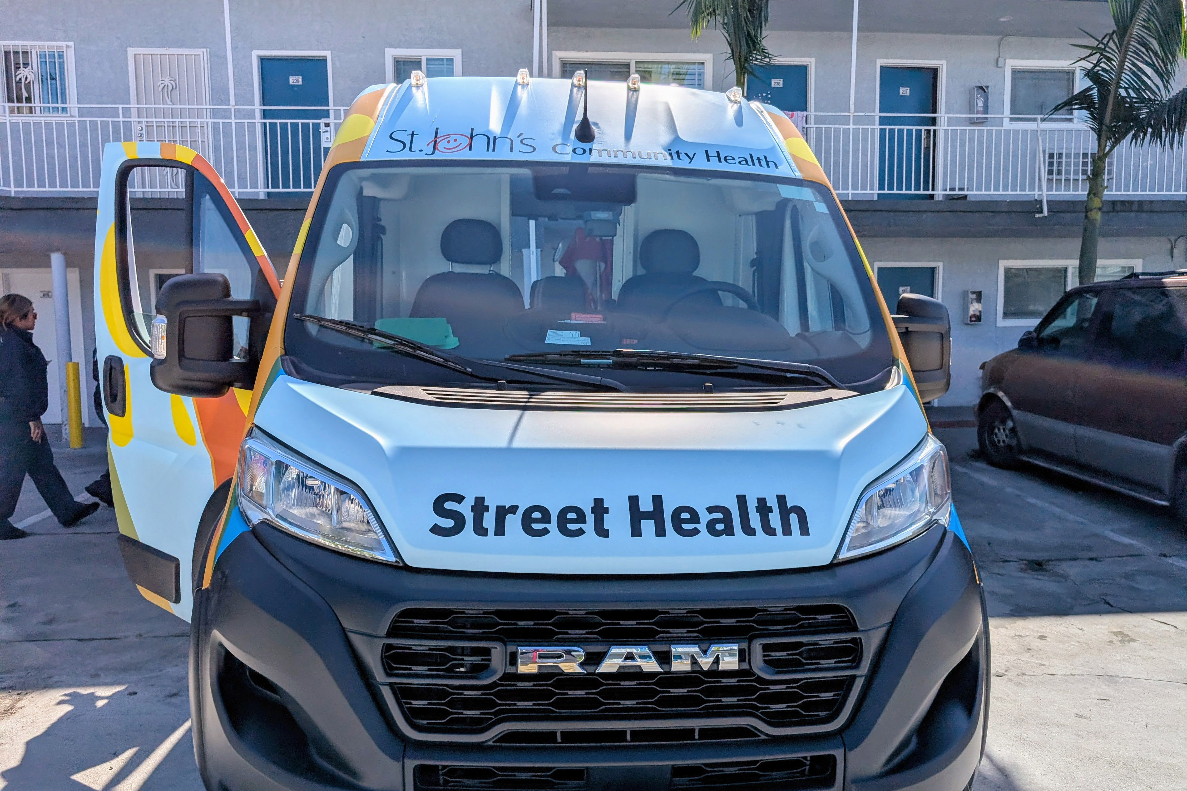A Dodge Ram van has logos for St. John's Community Health on it. The front of the van has the words "Street Health" on it.