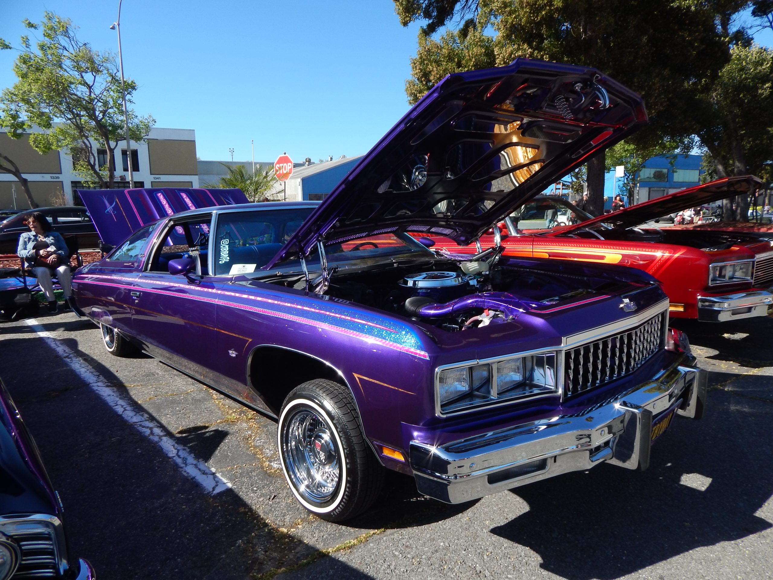 A purple classic Chevrolet car with its hood open, showcased at an outdoor car show; chrome details and custom paint visible.