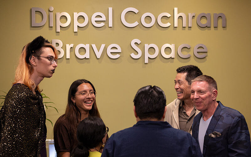 Students, staff and community supporters talk in front of the Dippel Cochran Brave Space sign