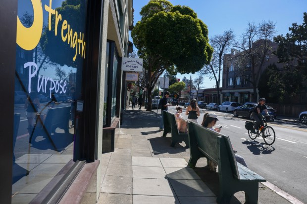 A bicyclist rides along College Avenue as passengers wait for a bus at a stop near the Rockridge BART station in Oakland, Calif., on Friday, March 6, 2026. The city of Oakland is considering building new housing units after a new California housing law permits homes to be built near public transit hubs. (Ray Chavez/Bay Area News Group)