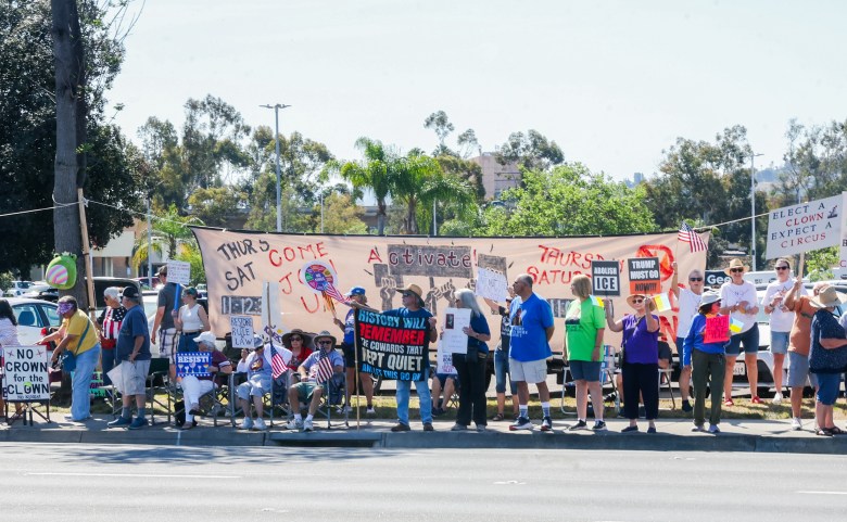 A diverse group of people protest on a sunny day, holding signs with messages advocating for change and justice, creating a lively and determined atmosphere.