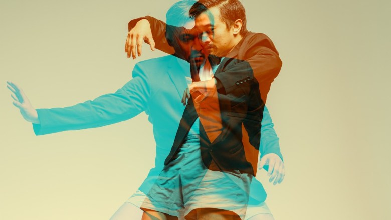 Overlapping images of two men in contrasting suits, one in blue and one in dark, set against a beige background.