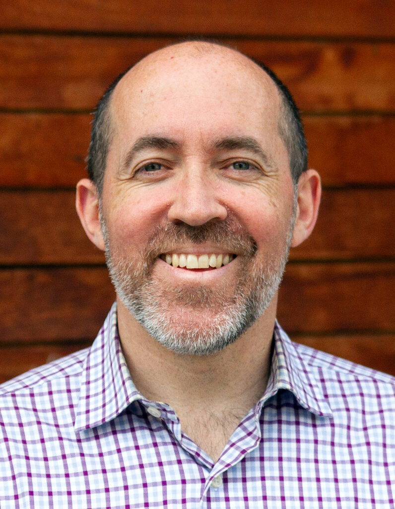 informal headshot of Evan B. White, with an open-collared shirt against a background of wood planking