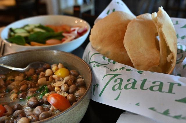 Chef’s Favas, a mixture of black fava beans and chickpeas in lemon olive oil sauce is seen to the left and pita bread to the right, one of many offerings at Zaatar Bistro, photographed Wednesday, April 10, 2024 in Fresno.