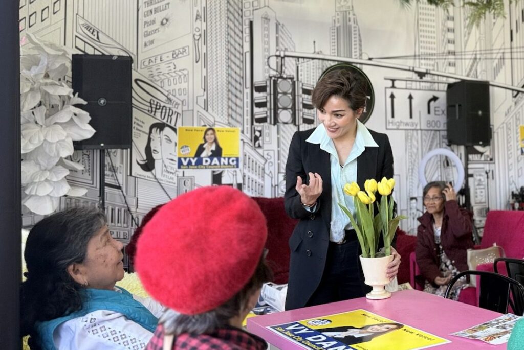 A women in a black blazer holding a pot of flowers speaks with two other women.