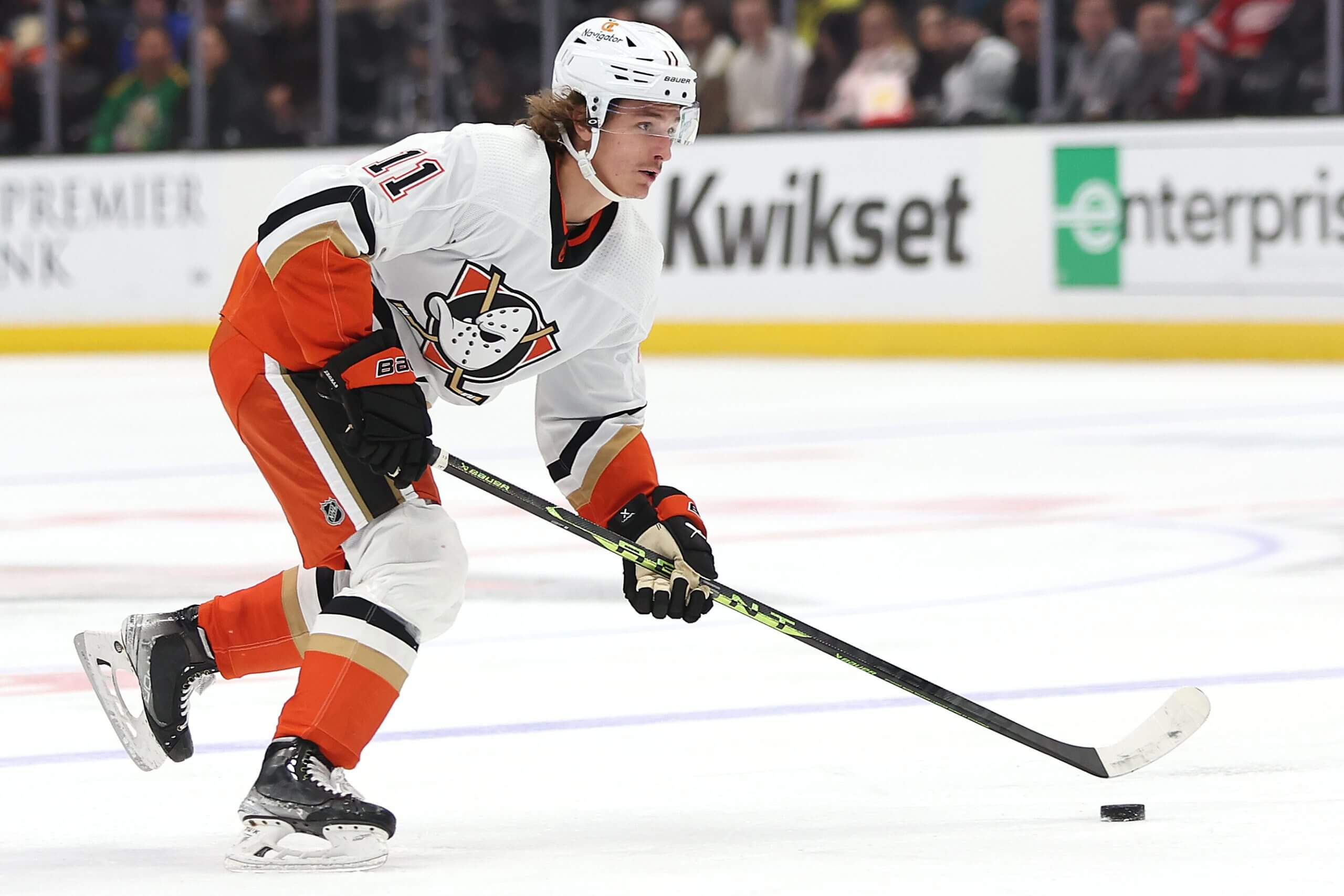 Trevor Zegras, in a white sweater, controls the puck.