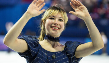 A young woman in a blue outfit and choker necklace waves to a crowd.