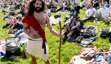 Man dressed in a costume holding a staff standing in a crowded park.