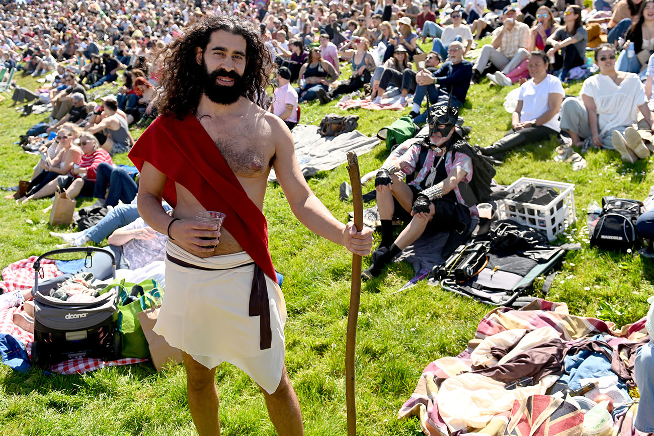 Man dressed in a costume holding a staff standing in a crowded park.