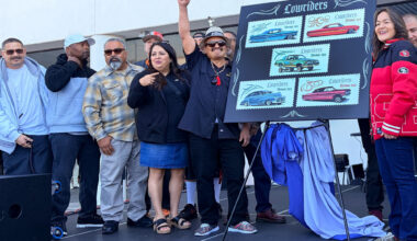 A group of Latino celebrants gather around an easel showing five stamp designs of lowrider-style cars