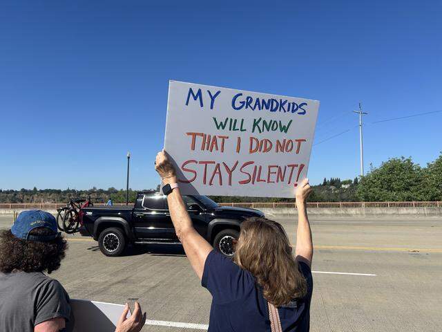 Julia Garland holds a sign for passing traffic on the Lake Natoma Crossing bridge in Folsom during a “No Kings” protest rally Saturday.