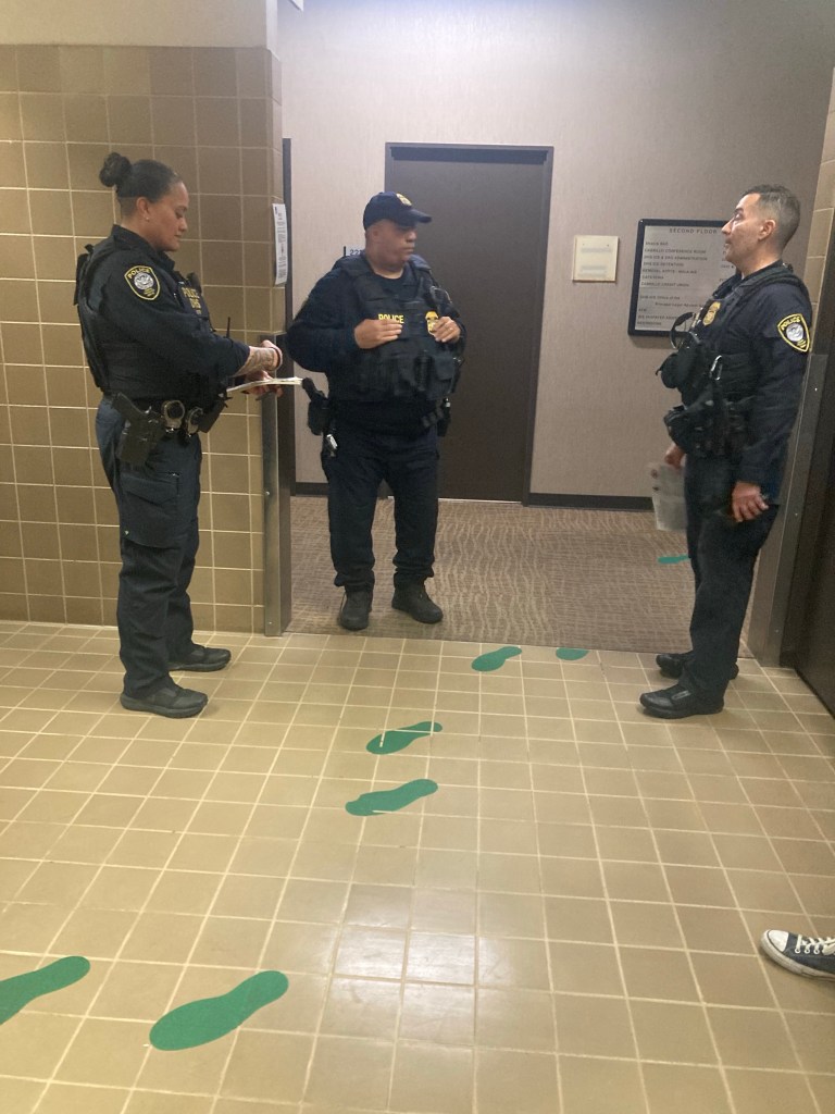 Three uniformed agents in a hallway with green footprints on the floor.