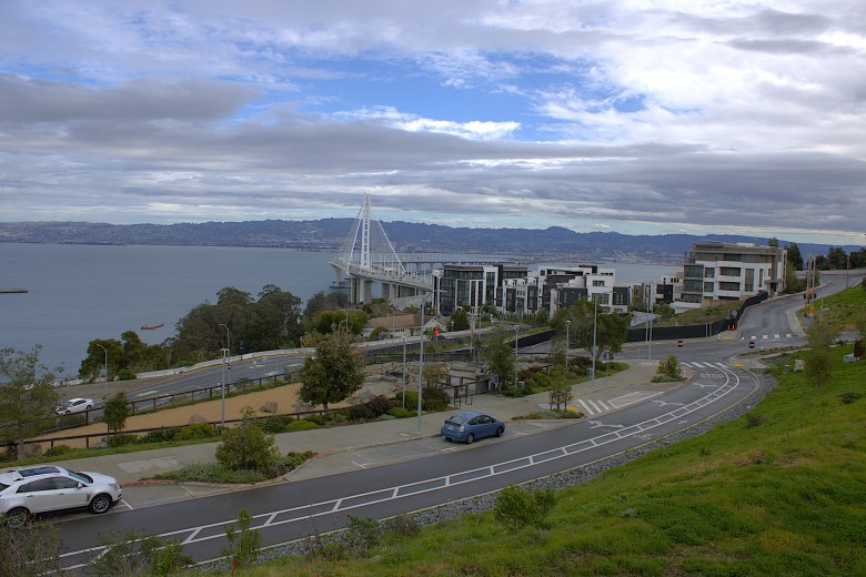 Landscape of hills, a road and buildings, with a tall bridge over a wide bay in the background