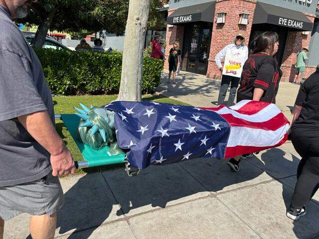 Protesters carry a piece of art that depicts a deceased Statue of Liberty covered in the American flag.