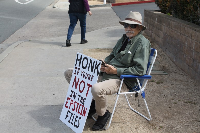 a senior man in a lawn chair with a sign that says "honk if you're not in the epstein files"