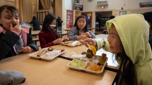 Emily Vang, 8, right, eats her school lunch other students in the cafeteria at Oak Ridge Elementary School in Oak Park on Wednesday, Feb. 22, 2023. Sacramento schools need federal support to buy locally grown produce, boost farmers and serve healthier meals.