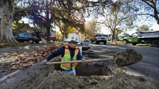 A worker digs a hole in Land Park as part of a water main replacement project in 2014.