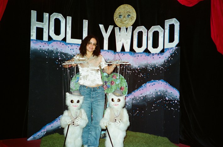 a woman in a white top and blue jeans puppeteering two white cats