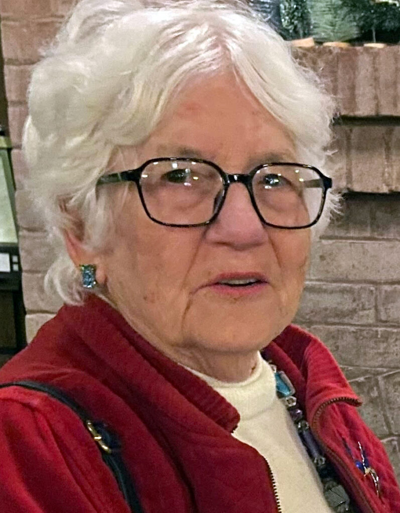 An informal portrait of Karen Merritt, wearing a red jacket and a cream-colored sweater.