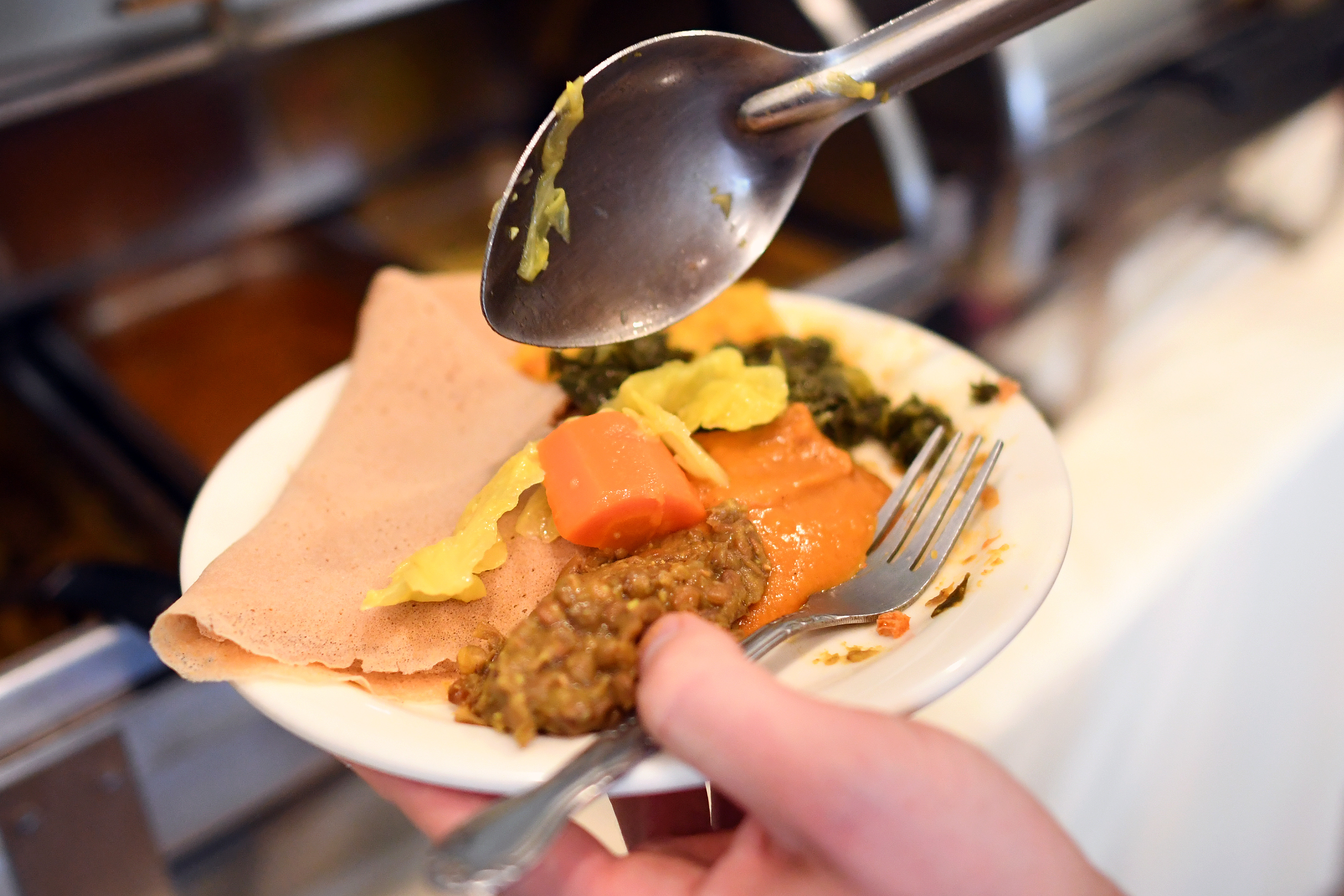 A patron fills a plate with plant-based Ethiopian dishes from...