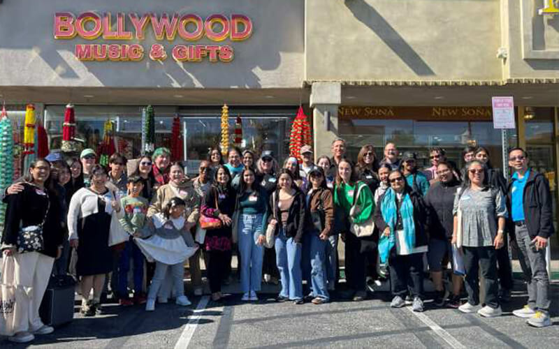 A group of students stand in front of a Bollywood Music and Gifts store in Little India