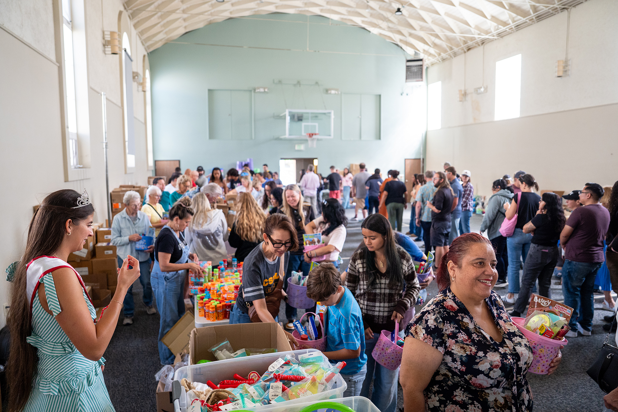 Volunteers move from table to table assembling Easter gift baskets...