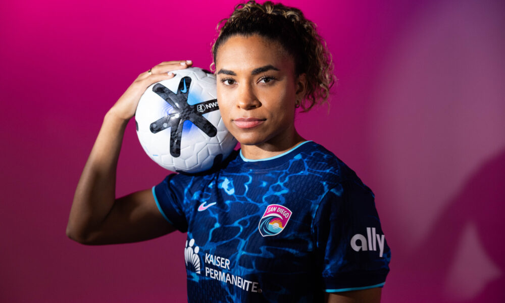 Catarina Macario wears a blue San Diego Wave jersey and holds an NWSL soccer ball.