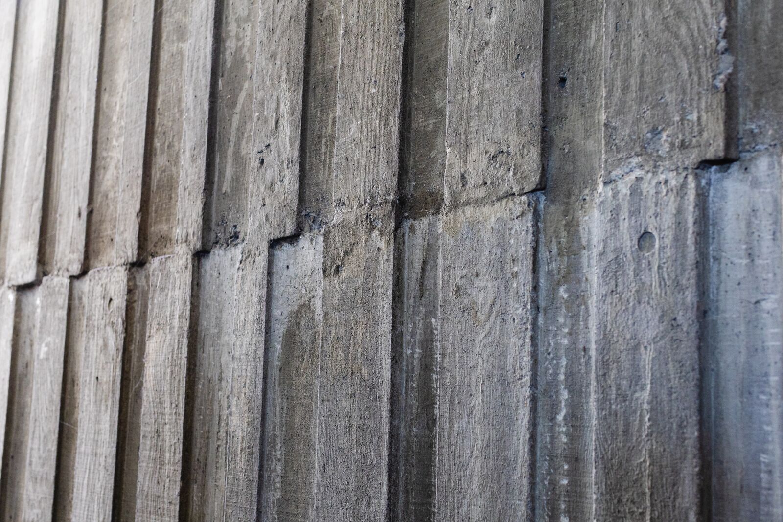A close-up view of a section of board-cast concrete. The gray material is made up of alternating panels, creating vertical lines.