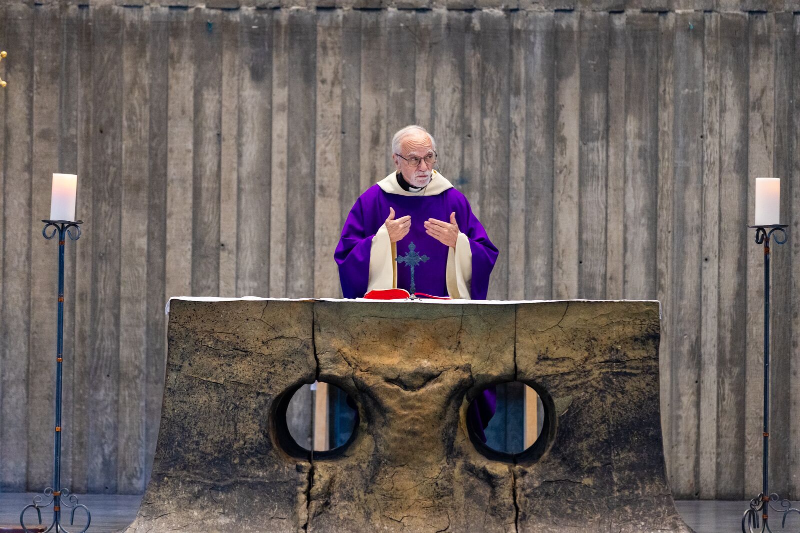 A priest in a purple robe preaches at an altar made of clay, with two large holes