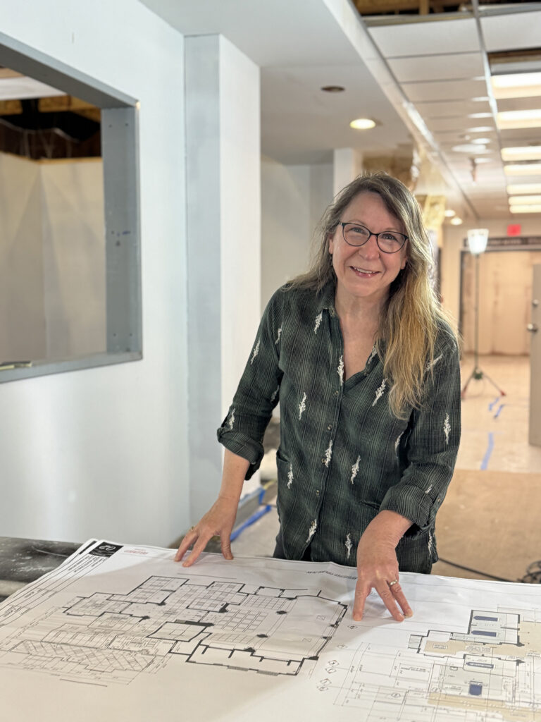 Production designer Nina Ruscio stands in the construction set of The Pitt, her hands resting on the show's designs for the trauma center.