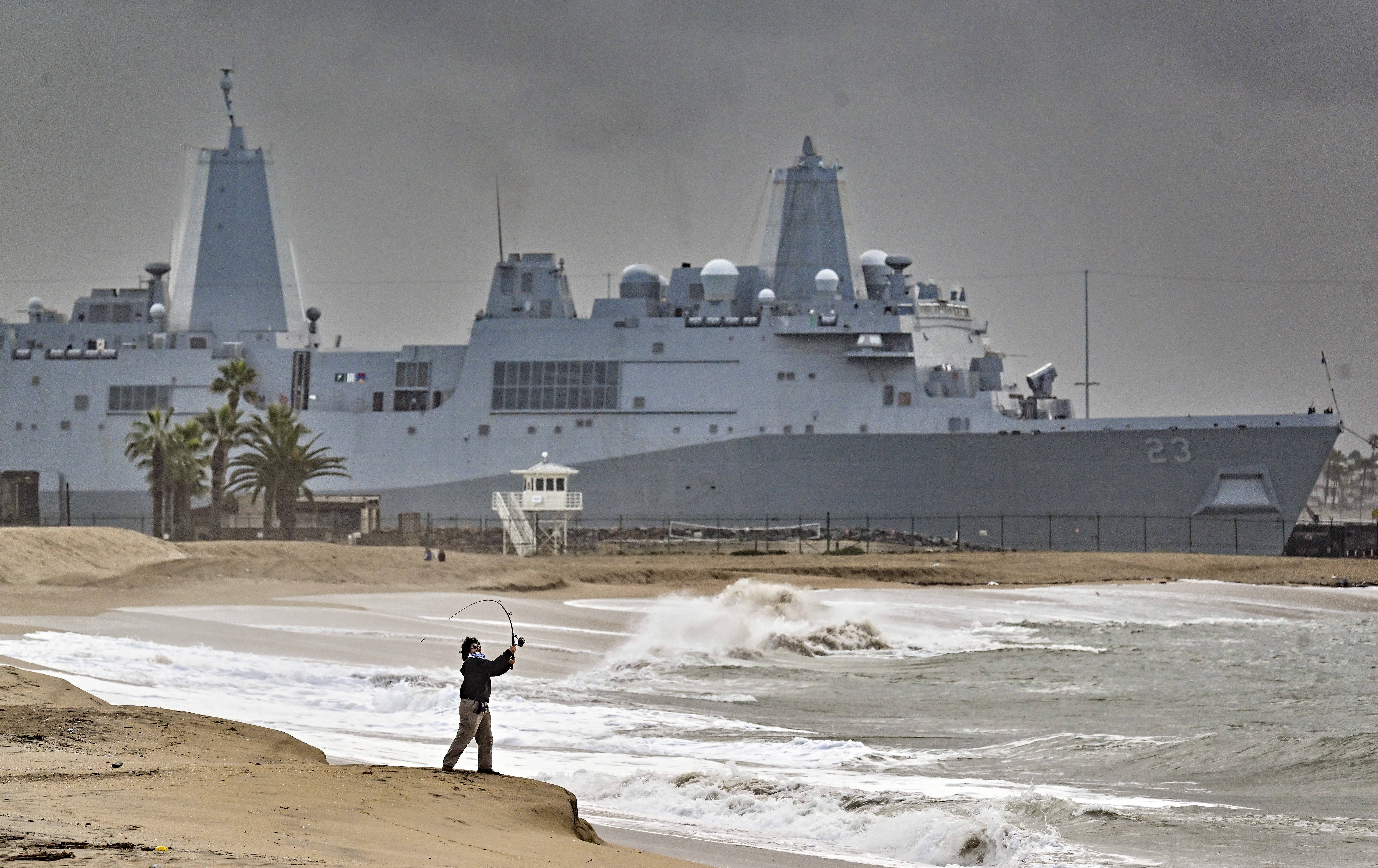 A beachgoer fishes south of the pier as USS Anchorage...