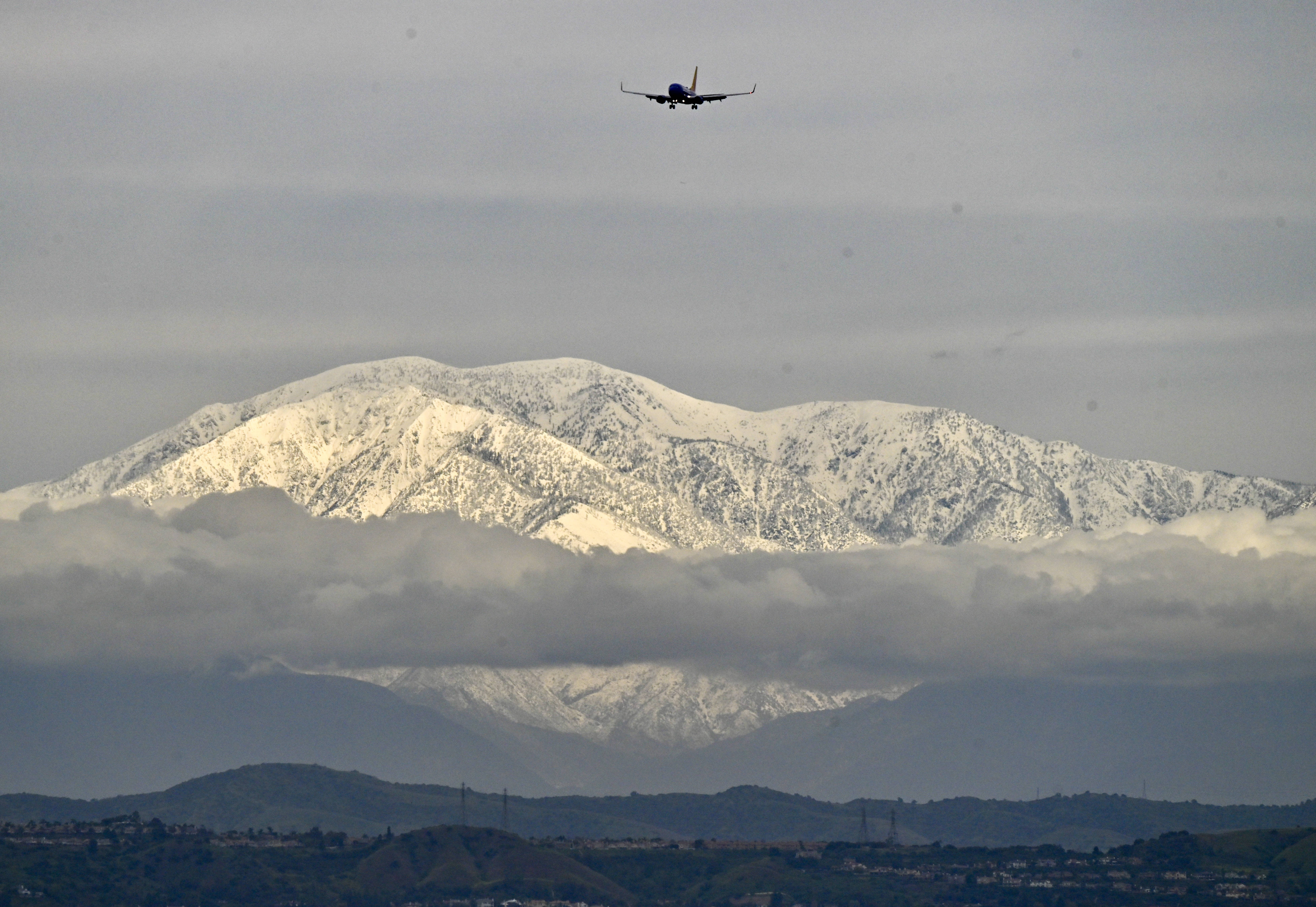 An airliner heads towards John Wayne Airport as snow cap...