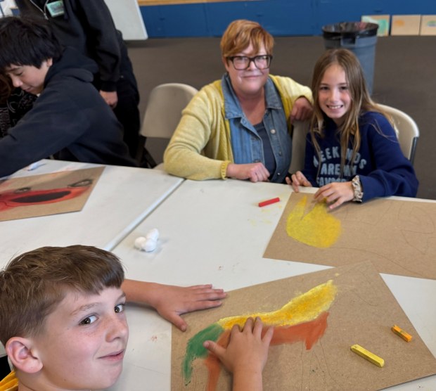 During a recent art lesson, Erin Pennell, admired the work of fourth graders, Fintan Kelly, lower left, and Lenora Mendlik. They were filling in large horse contours with pastels, influenced by the styles of Marc Chagall and Franz Marc who used horses extensively as symbols in their art work. (Cyril A Reinicke)