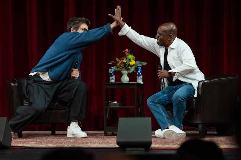 Photo of John Mayer and Greg Phillinganes high-fiving from their chairs on a stage.