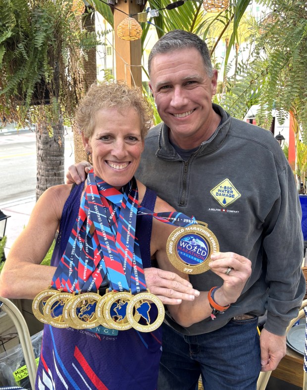 Tracy Roth and her husband, Brad, at the celebration lunch in Miami on Feb. 6 wearing all seven of her finisher medals and 2026 World Marathon Challenge medal. (Courtesy of Tracy Roth)