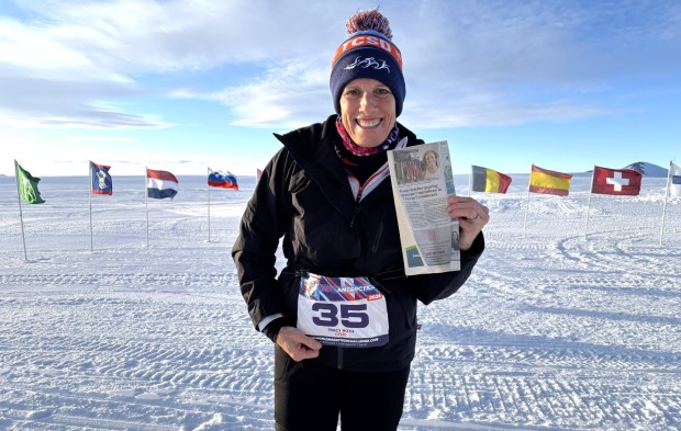 Tracy Roth in Antarctica on Jan. 31 holding a copy of the Oct. 30, 2025 Poway News Chieftain with the article about her fundraising for the 2026 World Marathon Challenge. Behind her are the flags of all 20 countries represented by the runners. (Courtesy of Tracy Roth)