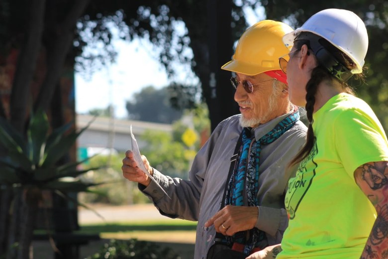 Two people in hard hats talking and examining a piece of paper outdoors.
