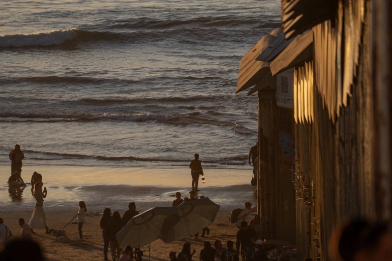 Families gather at a serene and beautiful beach with a huge wall running down the middle of it.