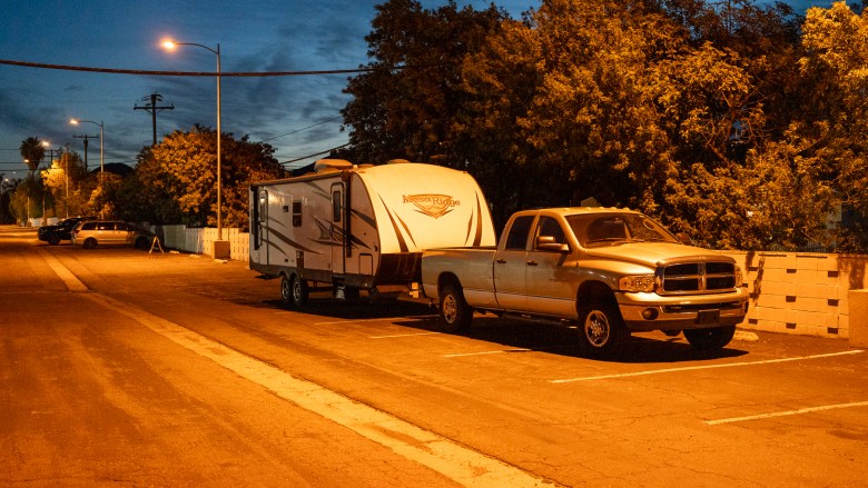 A truck towing a Mesa Ridge mobile camper is parked across multiple parking spaces. Orange street lights recede into the background of the image.