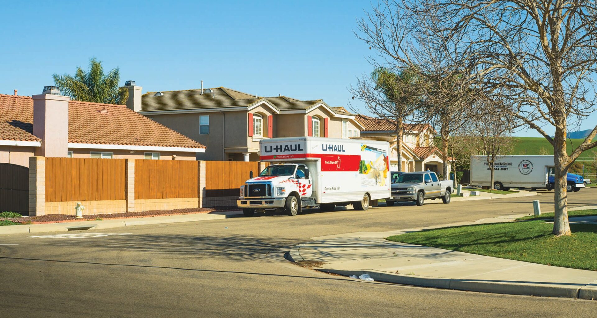 A Uhaul rental truck is parked on a neighborhood street, along with a truck, and a larger moving truck in the background.