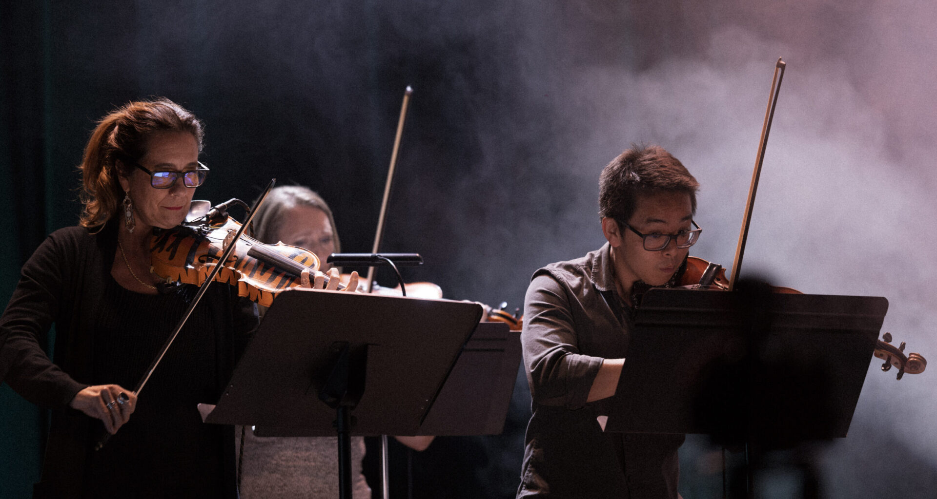 Three people play violin on a stage