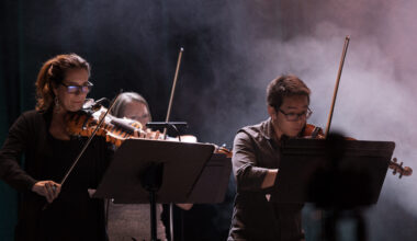 Three people play violin on a stage