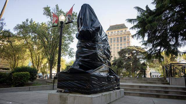 Black plastic covers the statue depicting Cesar Chavez in Cesar E. Chavez Plaza in Sacramento on Friday. City officials have announced plans to rename the park after accusations of rape and sexual assault by the civil rights leader surfaced earlier this week.